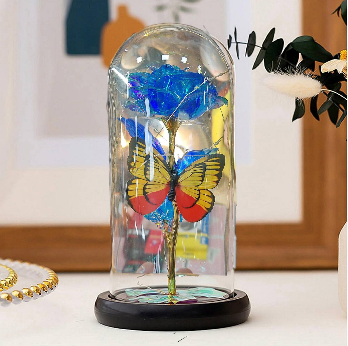 Plava večna ruža u staklenom zvonu sa žuto-crvenim leptirom