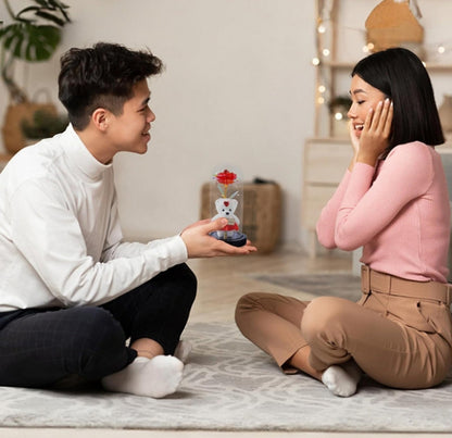 Romantični poklon za Dan zaljubljenih – staklena kupola sa ružom i medvedićem na drvenoj površini.